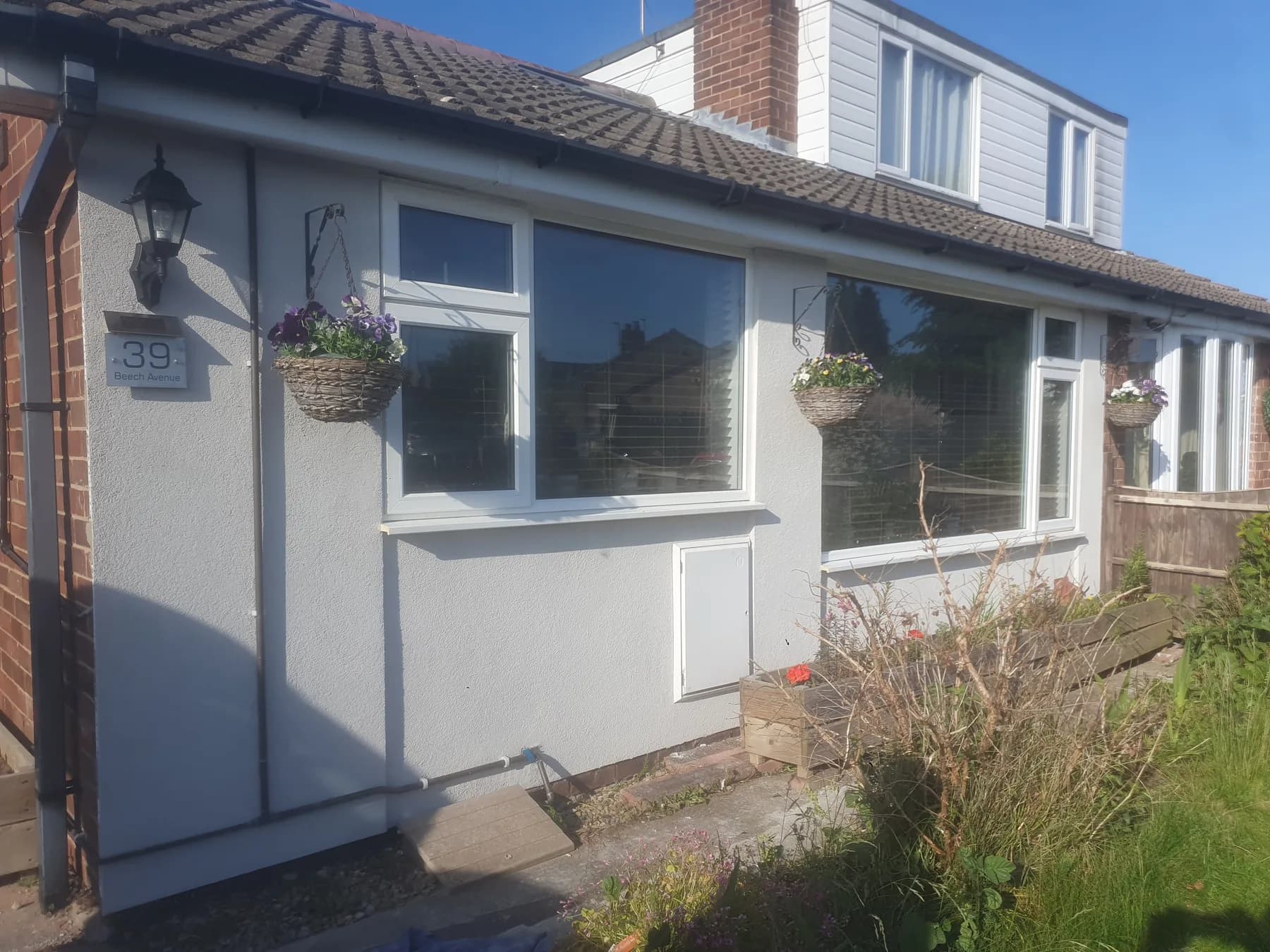 Bungalow extension after silicone render — light grey textured finish with blue sky