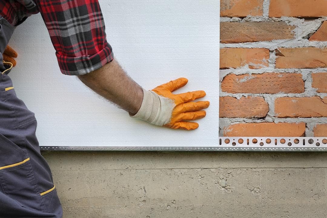 Installer pressing EPS insulation board against brick wall